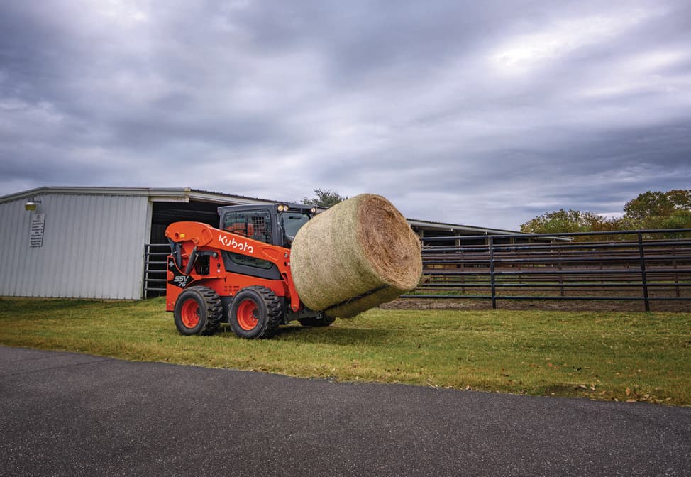 Kubota SSV75 lifting a hay bale
