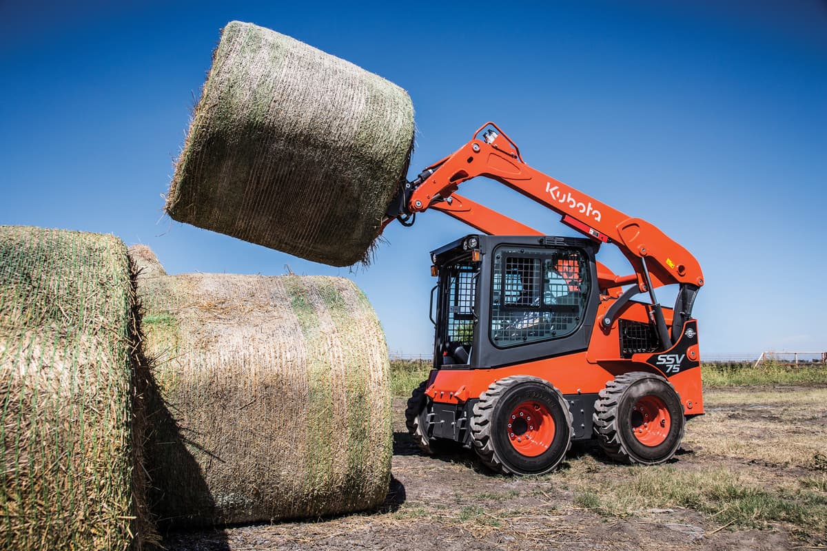 Kubota SSV75 lifting a hay bale